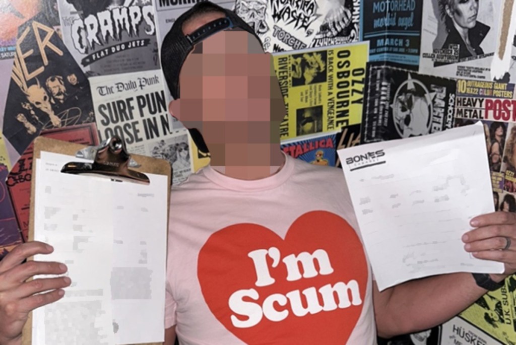 a picture of a man in a pink t-shirt with a heart that says "i'm scum." he wears a backward hat and his face is blurred. he holds up paper documents