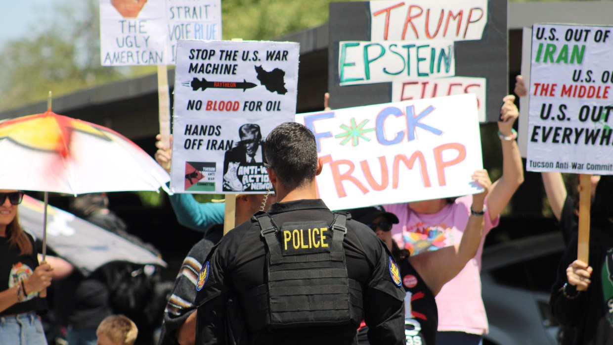anti-trump protesters hold signs in front of a phoenix police officer