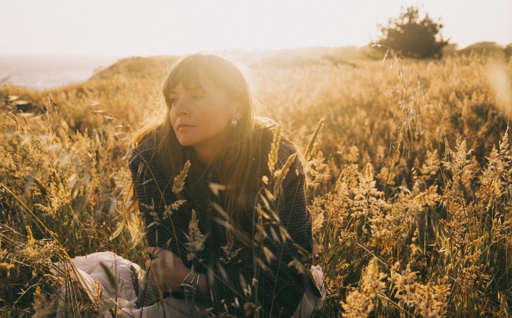Indie singer-songwriter Courtney Marie Andrews poses in a grass field at sunset for a publicity photo.