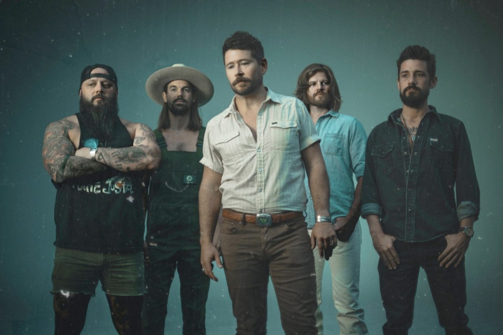 The members of Shane Smith and the Saints pose for a publicity photo against a dark blue background.
