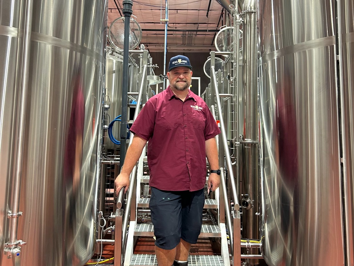 A brewmaster stands among brewing tanks.