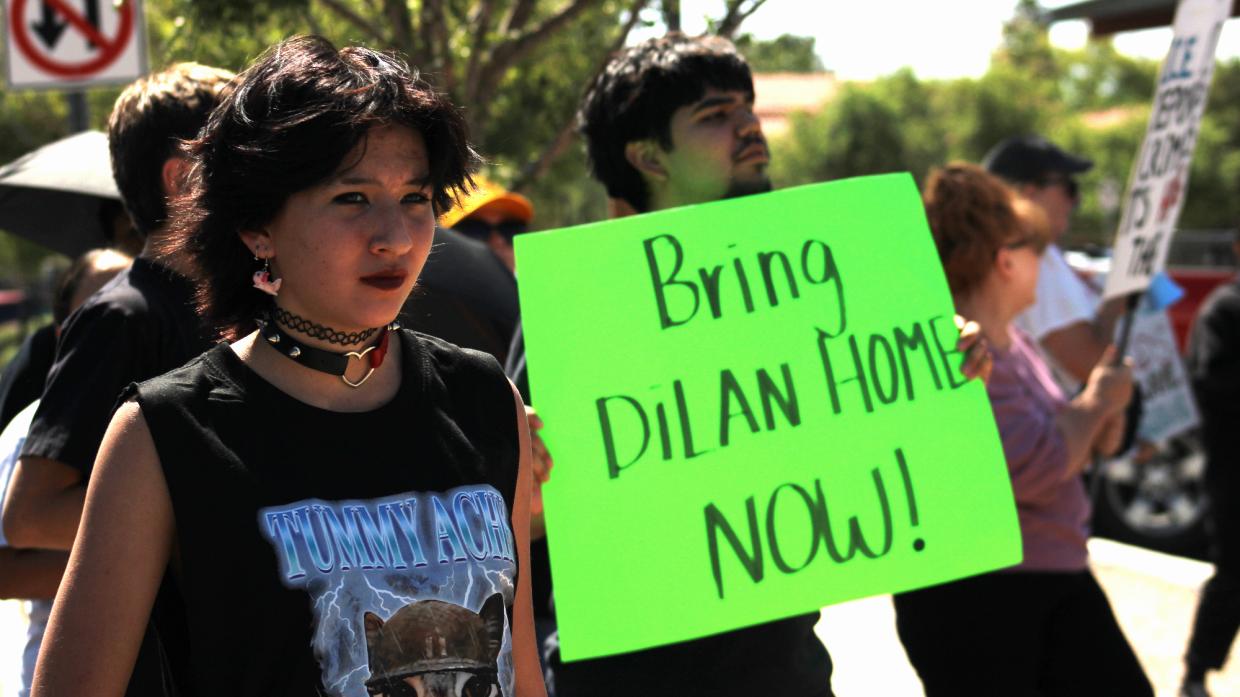 students at a protest. one holds a neon sign that says "bring dilan home now"