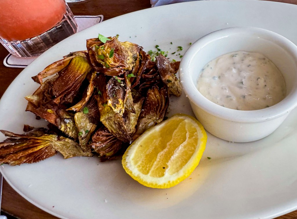 A plate of fried artichokes with a lemon wedge and dipping sauce.