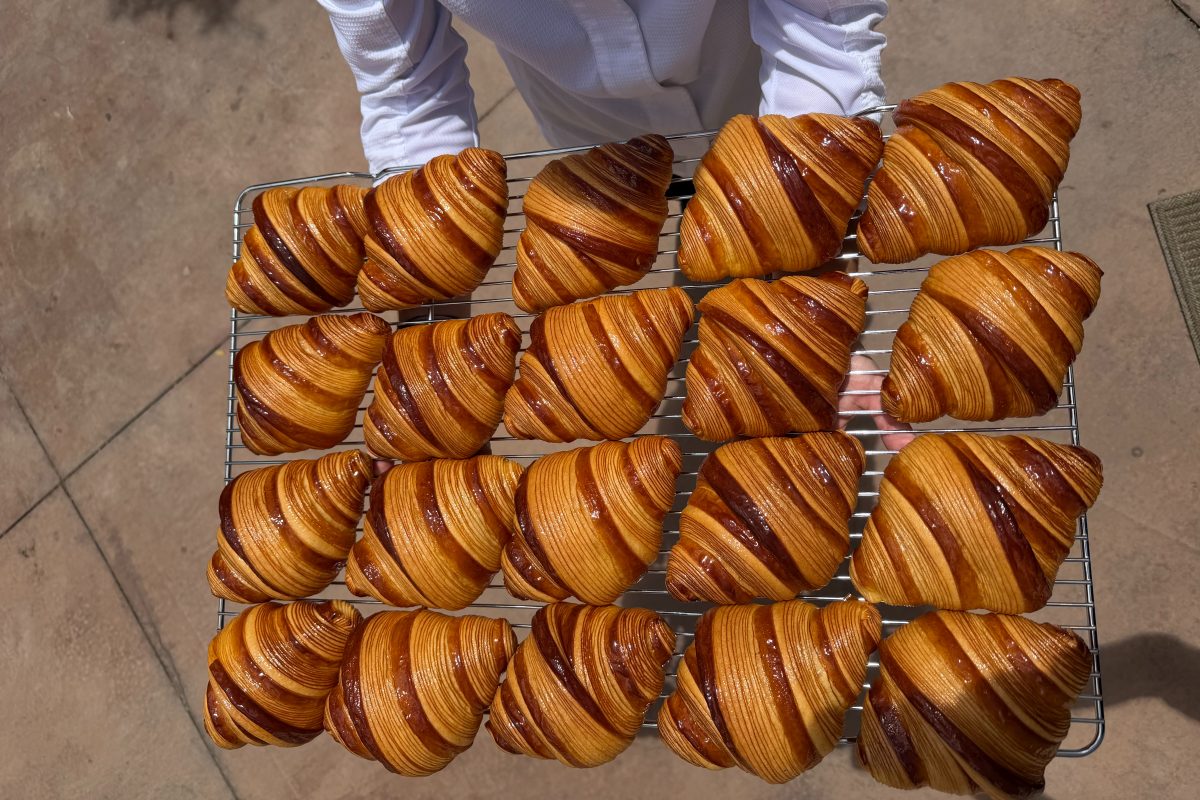 A person holding a rack with 20 glossy croissant.