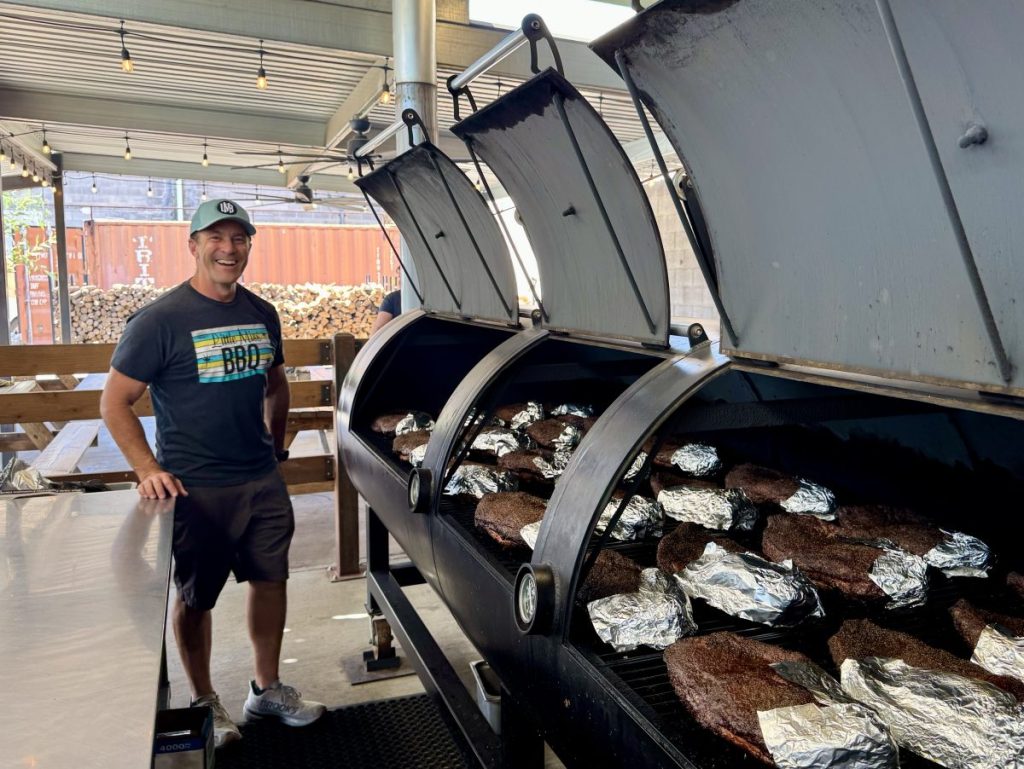 Little Miss BBQ owner Scott Holmes in front of open tank smokers filled with brisket.