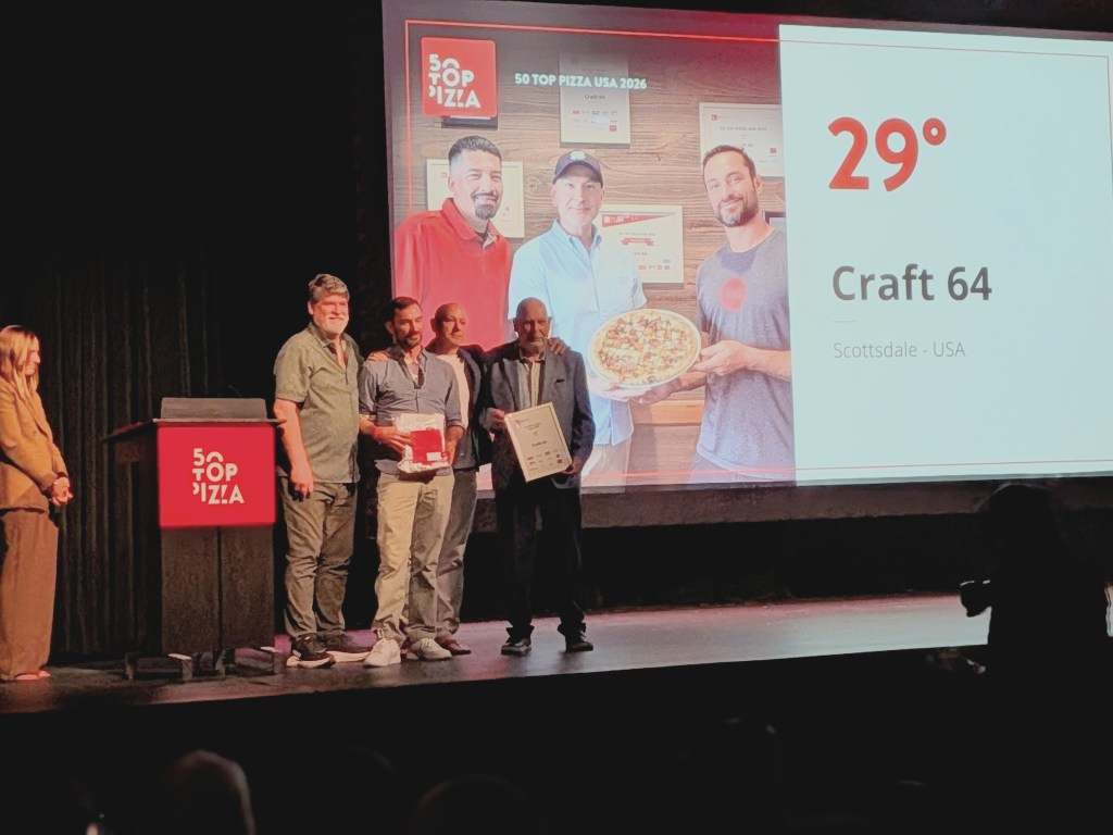Representatives from Craft 64 on a stage receiving their 50 Top Pizza award plaque.