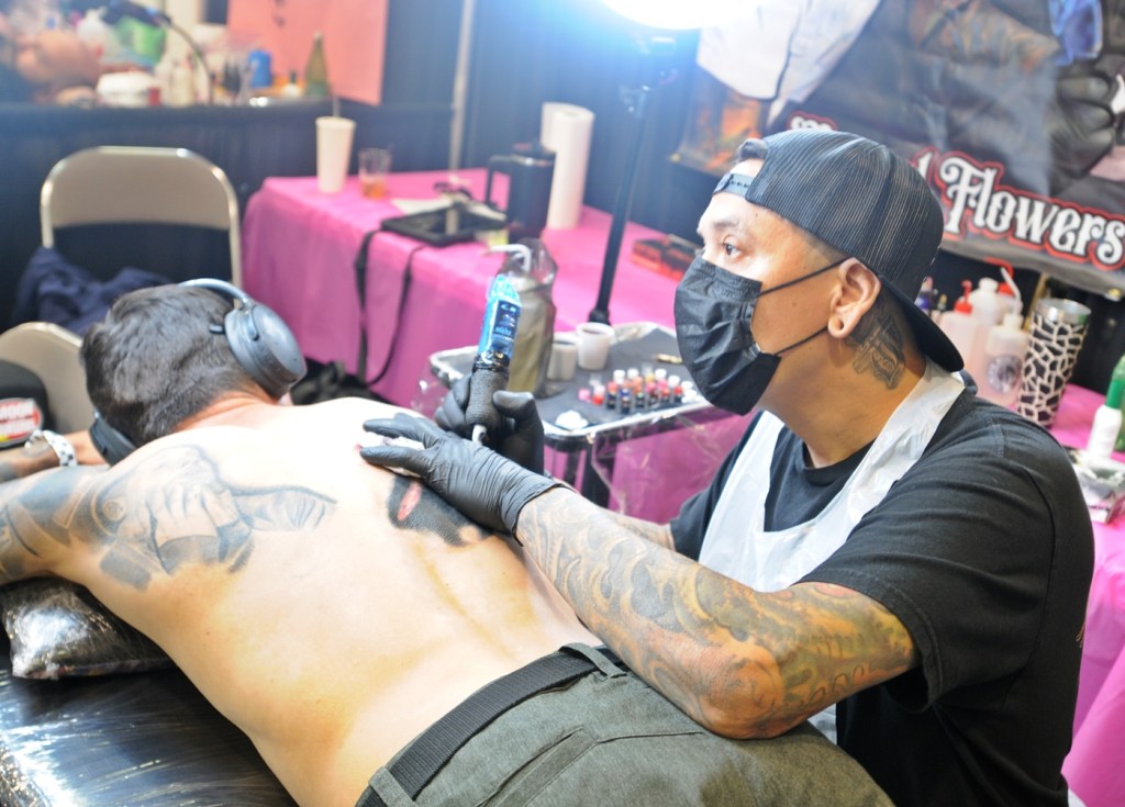 A tattoo artist inks a client at a tattoo convention.