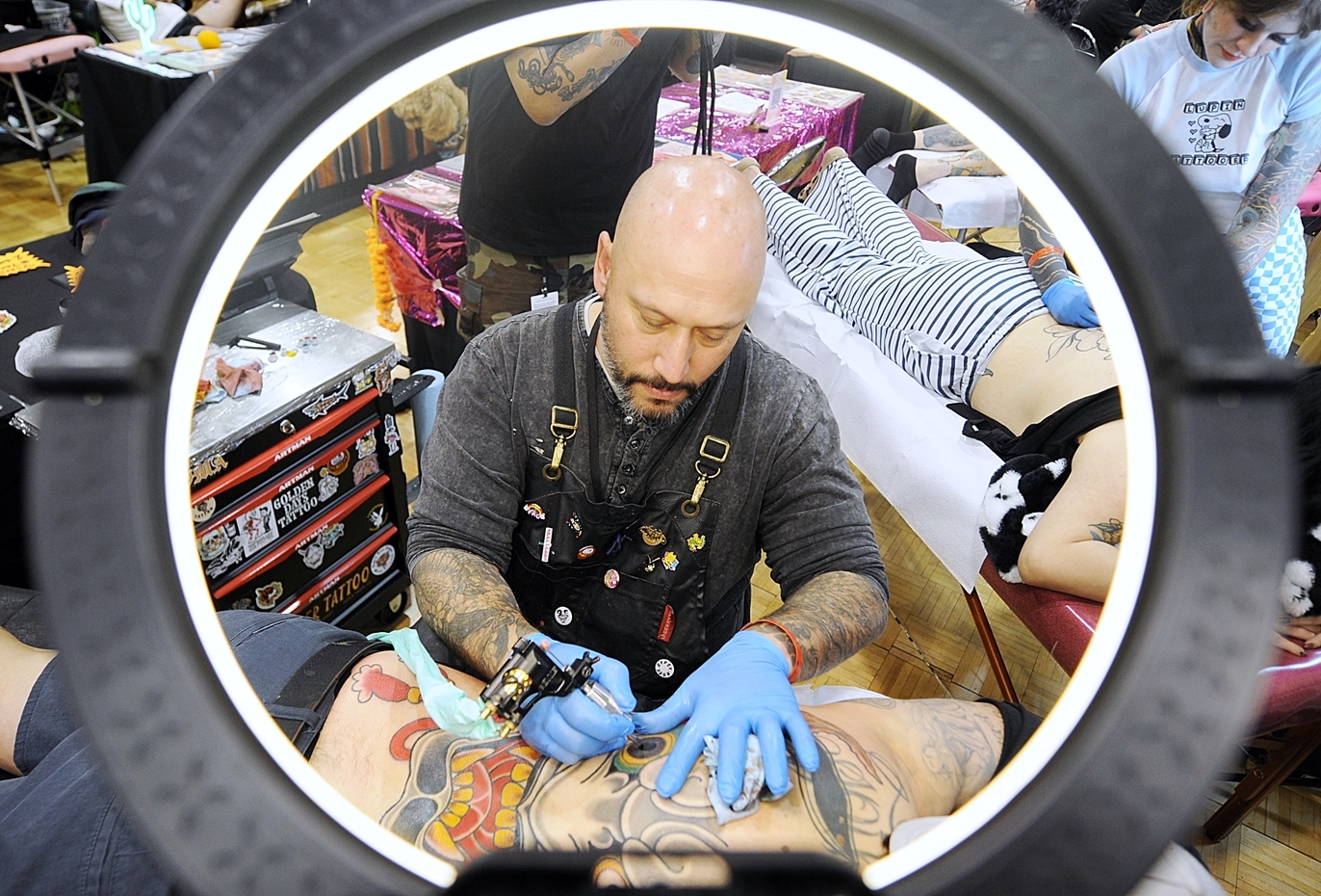 A tattoo artist inks a client at a tattoo convention.