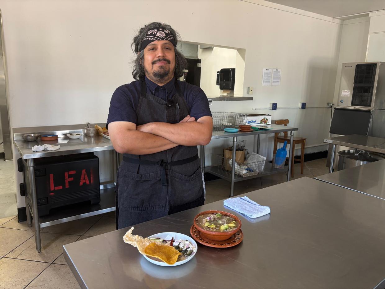 Chef Erick Pineda stands with a bowl of pozole and platter of accompanying toppings and snacks.
