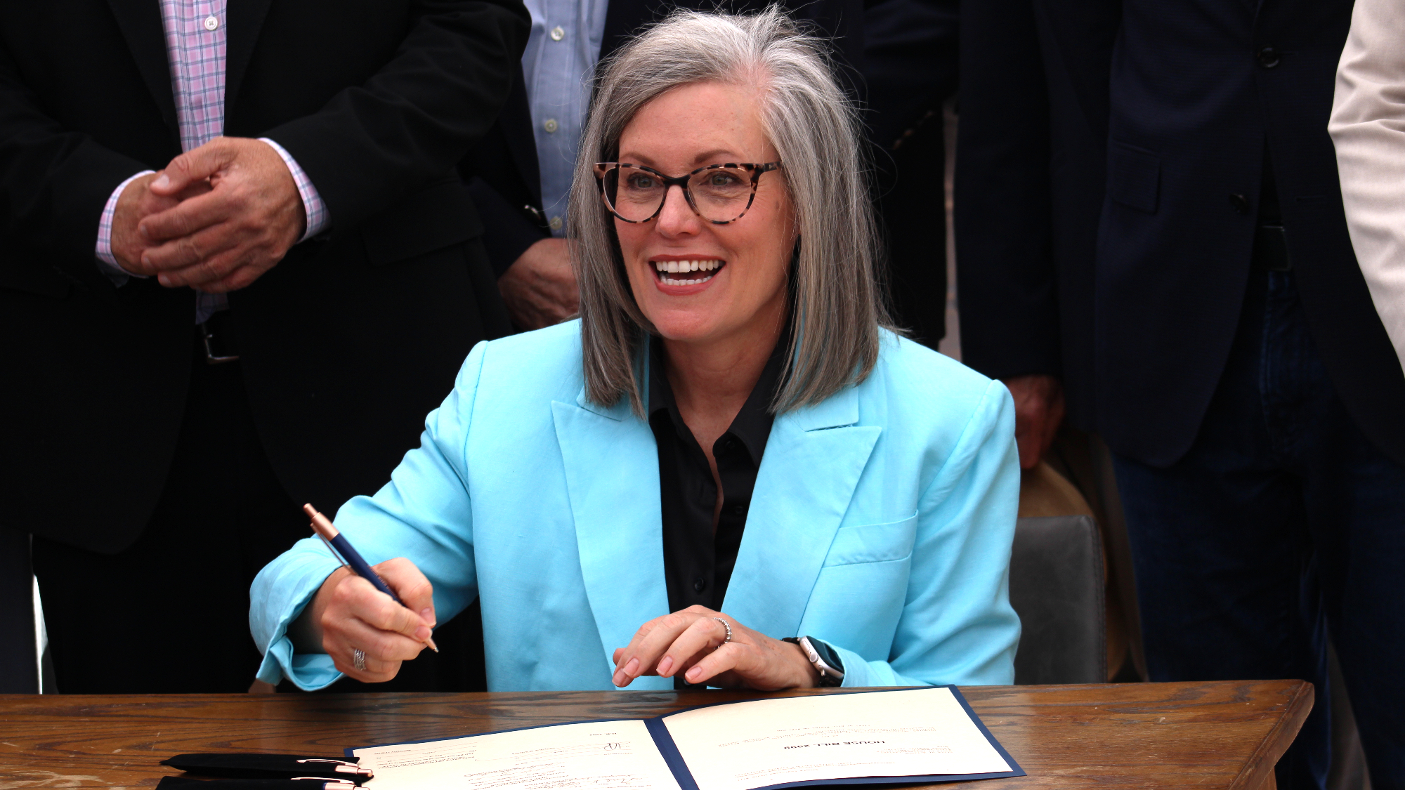 katie hobbs holds a pen while sitting at a desk and preparing to sign a bill
