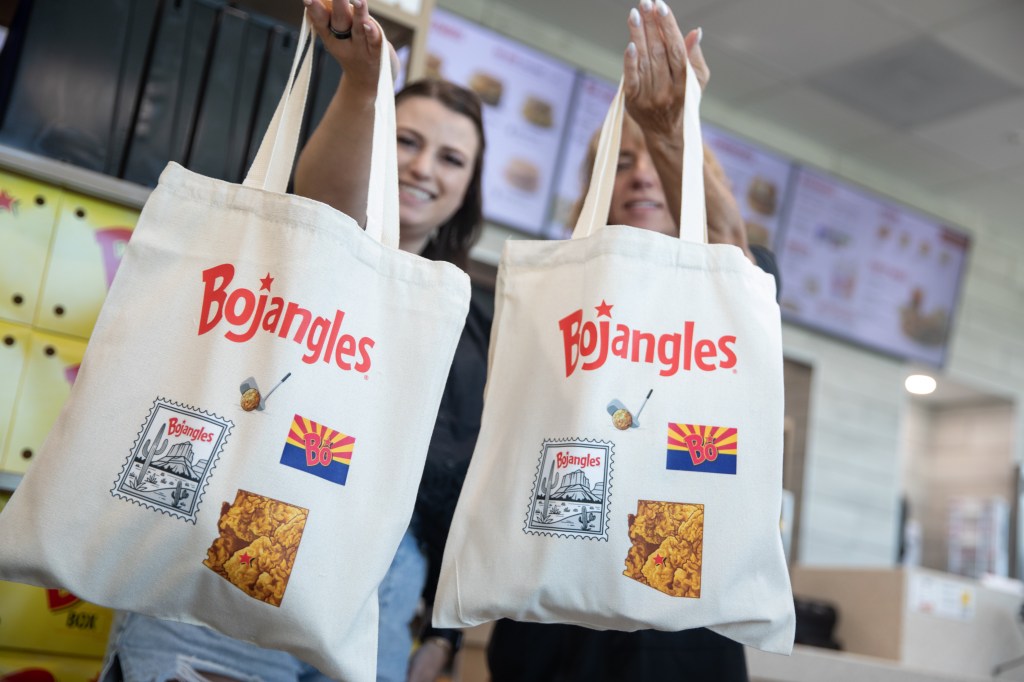 Two women hold Bojangles branded tote bags.