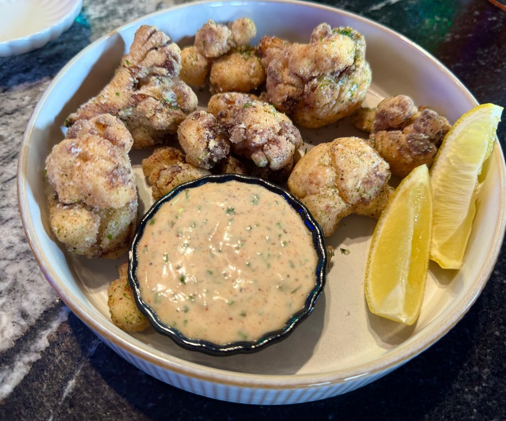 A platter filled with fried cauliflower, a dish of remoulade and lemon wedges.