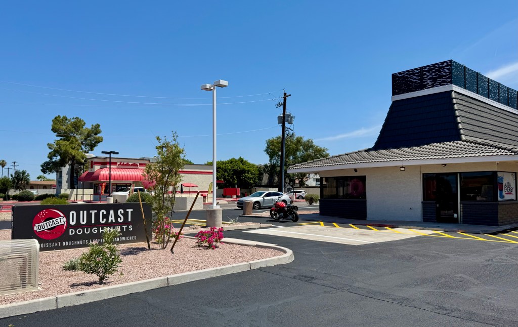 Outside the Scottsdale drive-thru of Outcast Doughnuts, with a view of its sign and the building.