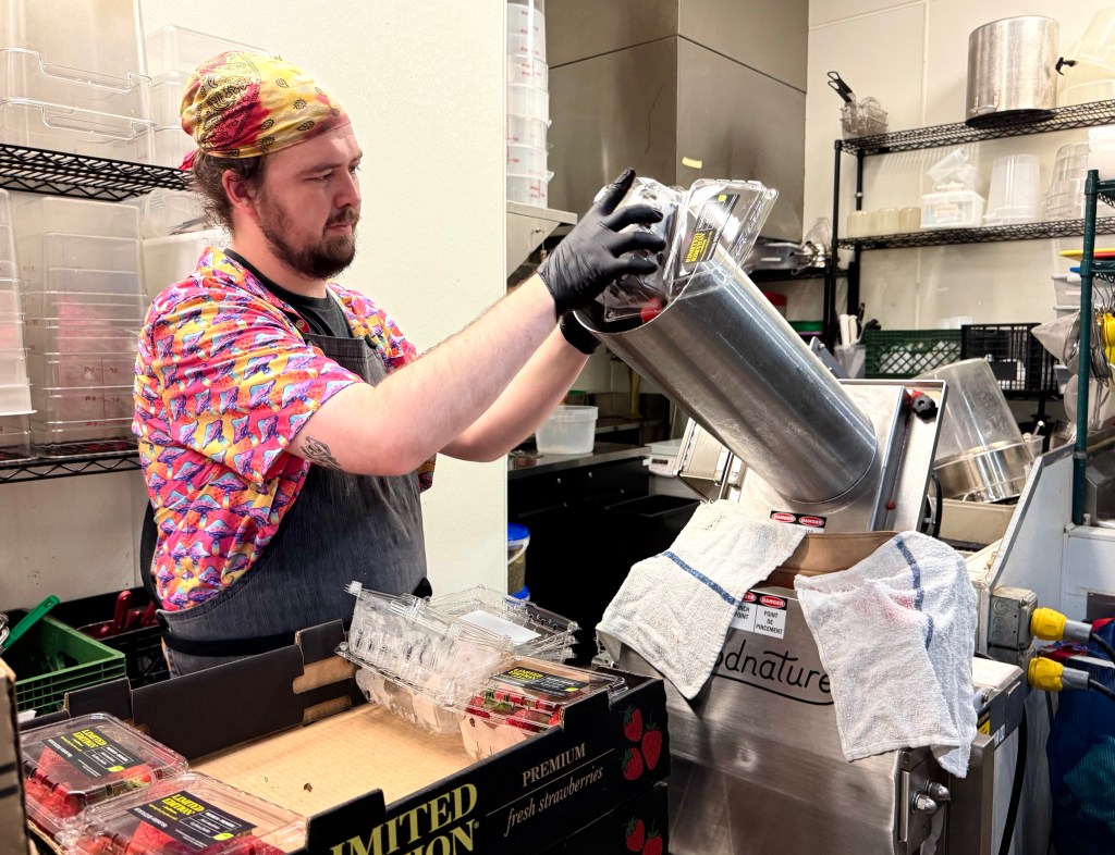 Chef Andrew Fouser feeds strawberries into a cold press juicer in the kitchen at Century Grand.