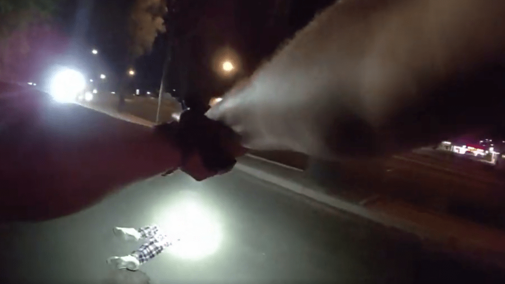 body-cam still showing two arms holding a gun on someone on the ground at night. only the person on the ground's legs are visible