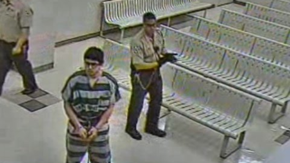 a man in prison stripes and handcuffs is seen in front of empty metal benches in security footage