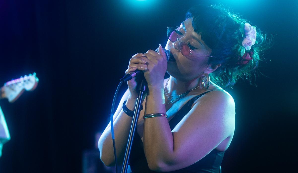 Arizona singer-songwriter Ang Sirena performs onstage with a microphone during a live concert.