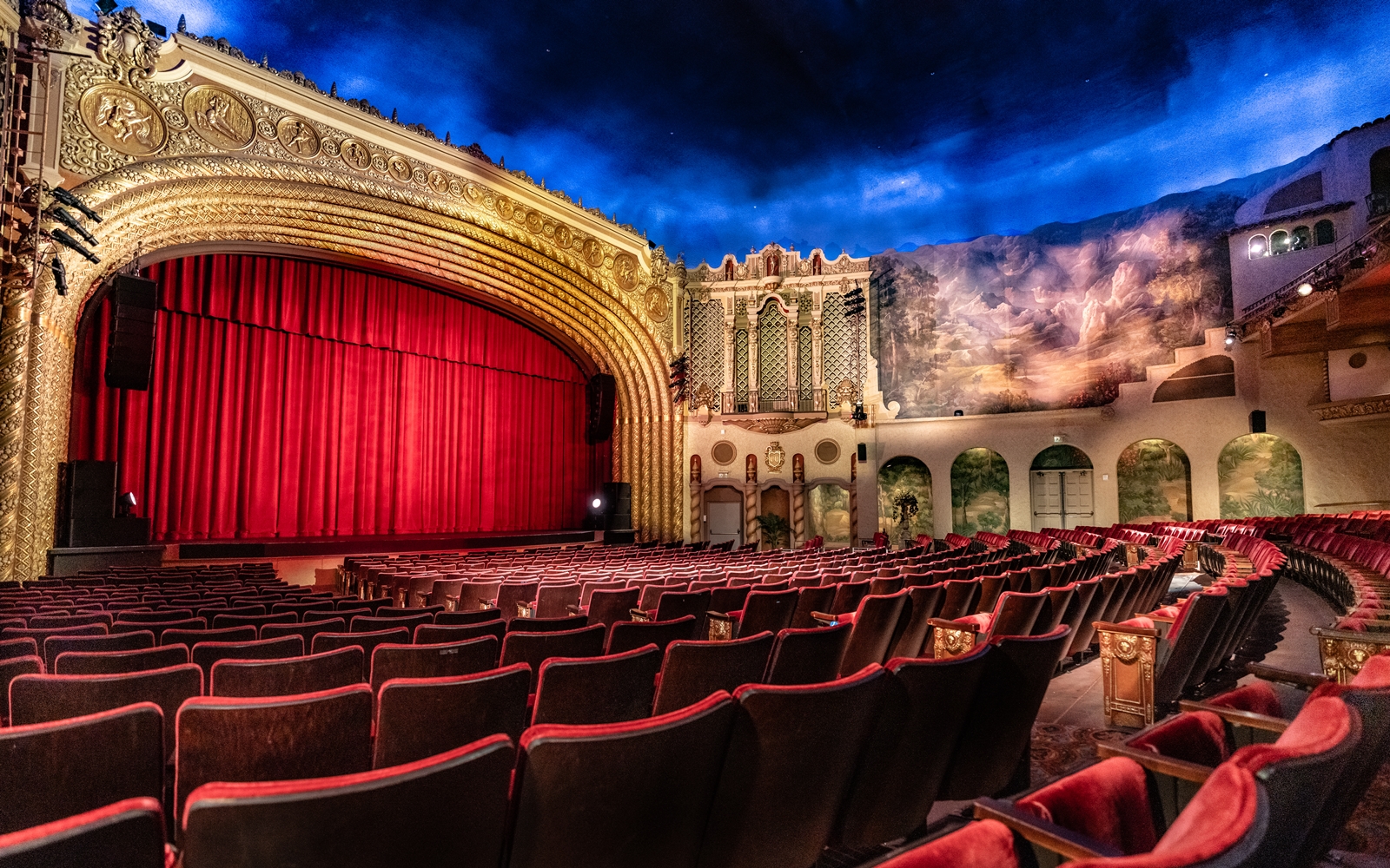 The ornate interior of the Orpheum Theatre in downtown Phoenix, featuring its gold proscenium arch, red velvet seats and painted blue sky ceiling.