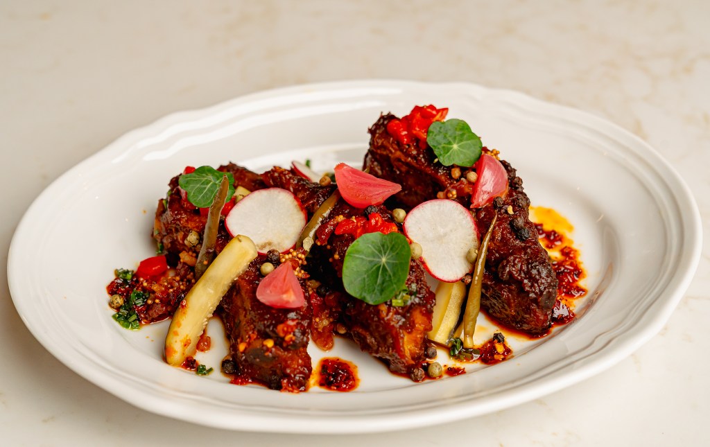 Three pork spare ribs on a plate that's garnished with pickles, chiles and microgreens.