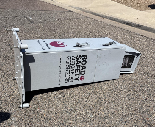 A destroyed and toppled speed camera lies desultorily on the pavement.