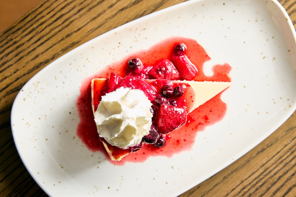 The overhead view of a slice of cheesecake topped with fruit and whipped cream.