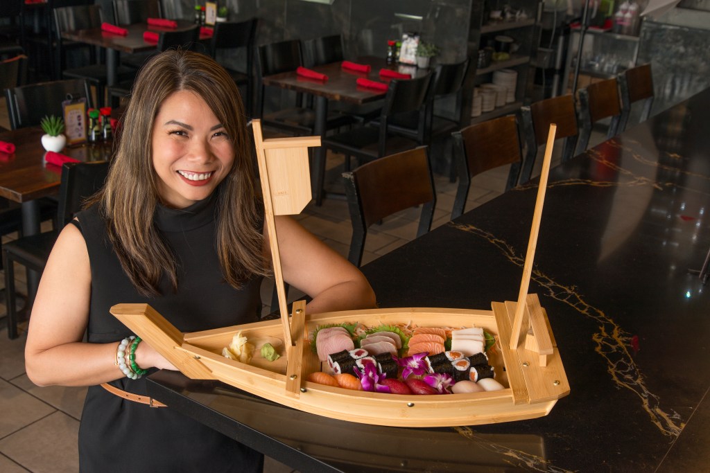 Kelly Yu shows off a spread of sushi in a wooden boat shaped container.