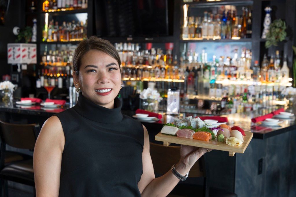 Kelly Yu holds a wooden board of sushi rolls.