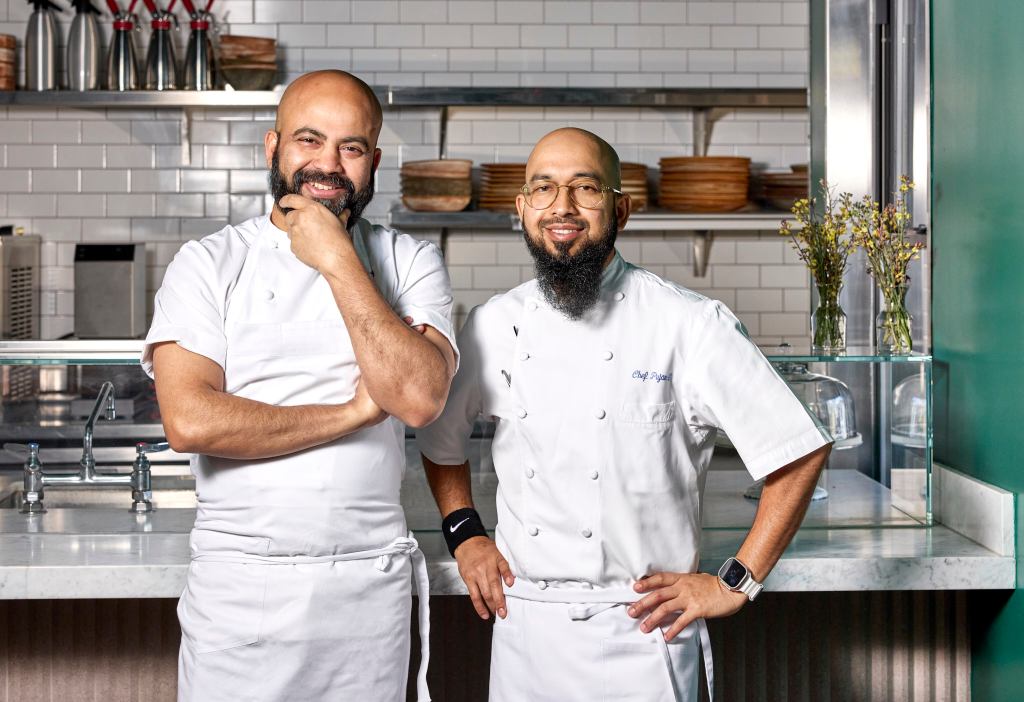 Chefs and brothers Sujan and Pujan Sarkar pose together in a kitchen.