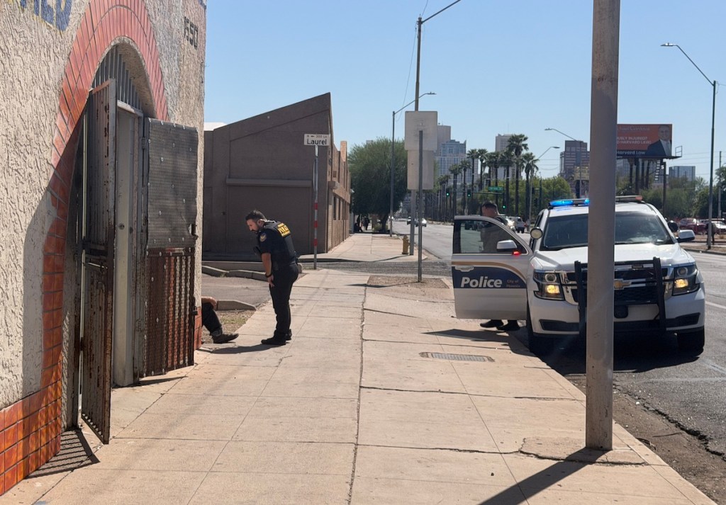 A police officer stops a homeless person on the sidewalk