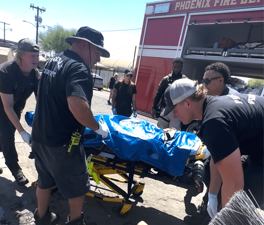 four Phoenix firefighters move a gurney with a blue cooling bag