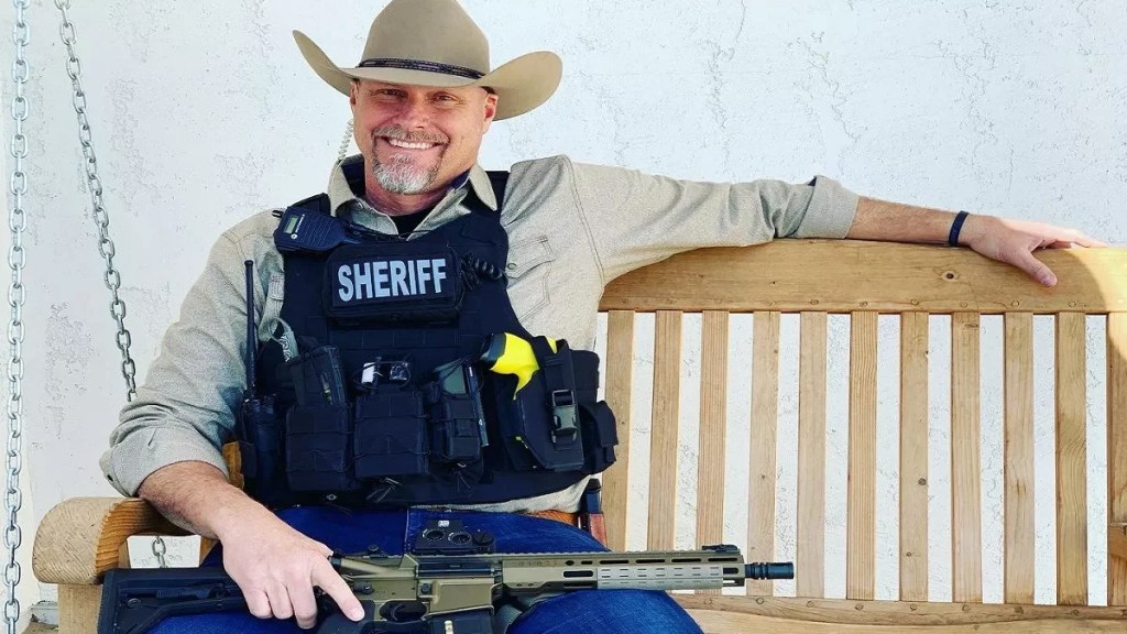 mark lamb in a cowboy hat with a rifle across his lap