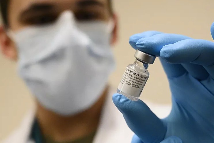 a masked medical worker holds a vial of covid-19 vaccine