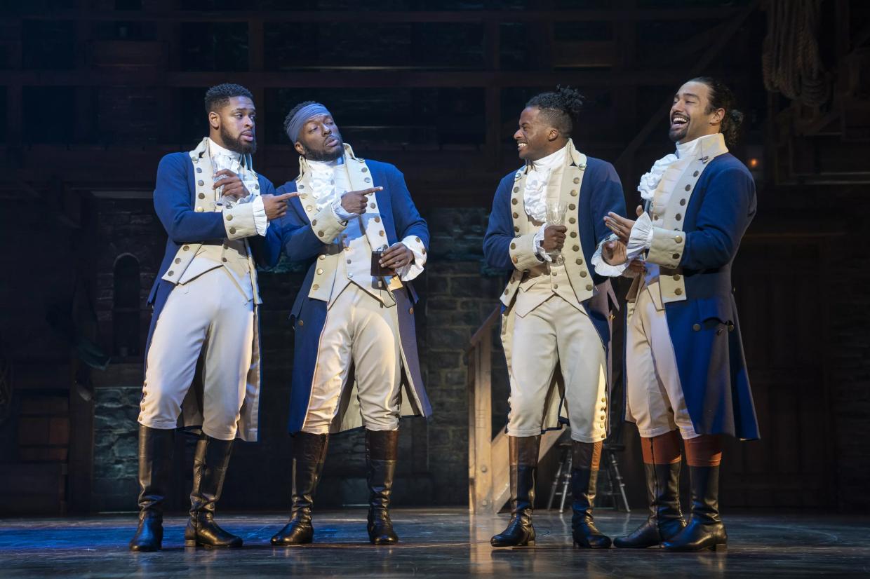 Four men dressed in old-fashioned clothes standing together on a stage.