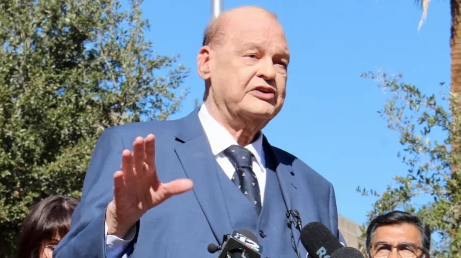 tom horne speaks at a press conference with jake hoffman standing behind him