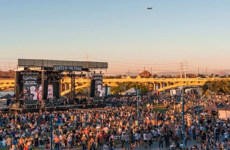 A large crowd gathered in front of a giant outdoor stage with a banner that says "Boots in the Park" across the top.
