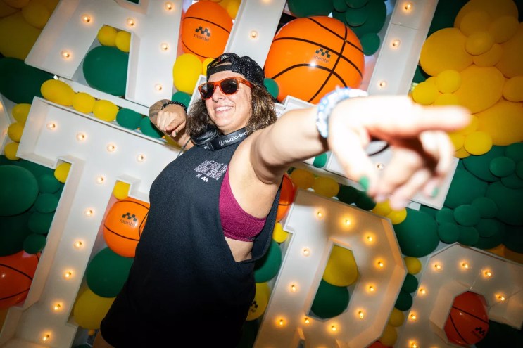 a woman points at the camera in front of an "All Stars" sign with balloons