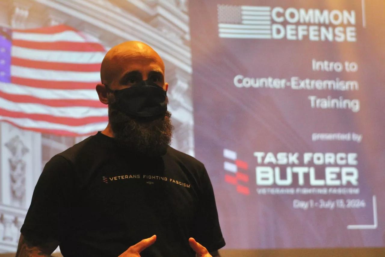 A man in a face mask speaking in front of a screen
