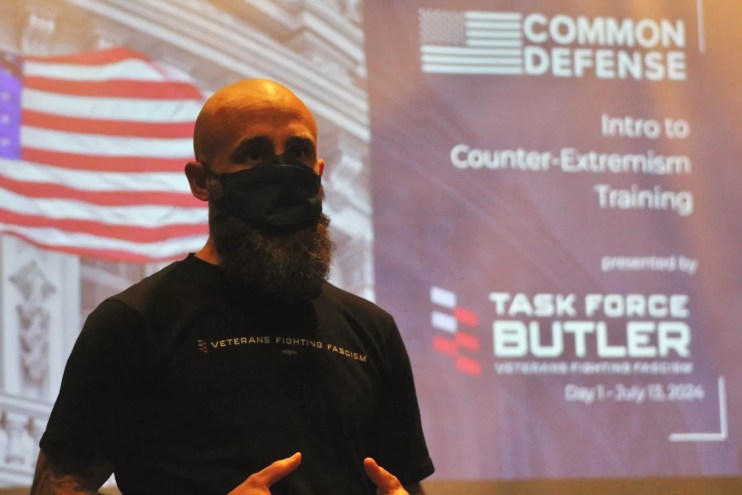 A man in a face mask speaking in front of a screen