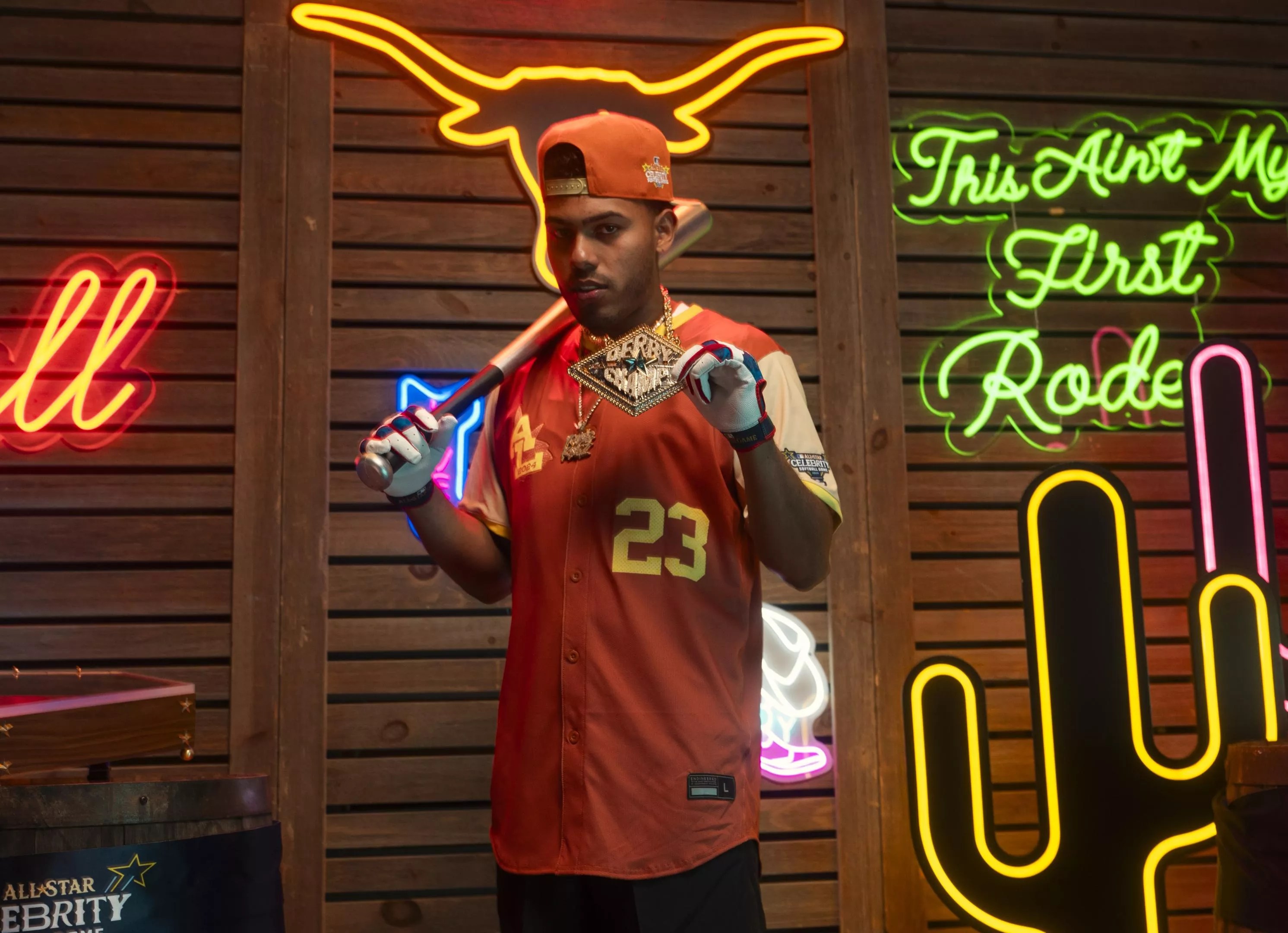A man in a baseball jersey in front of a wall of neon signs.