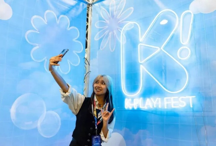 A young woman taking a selfie in front of a blue screen.