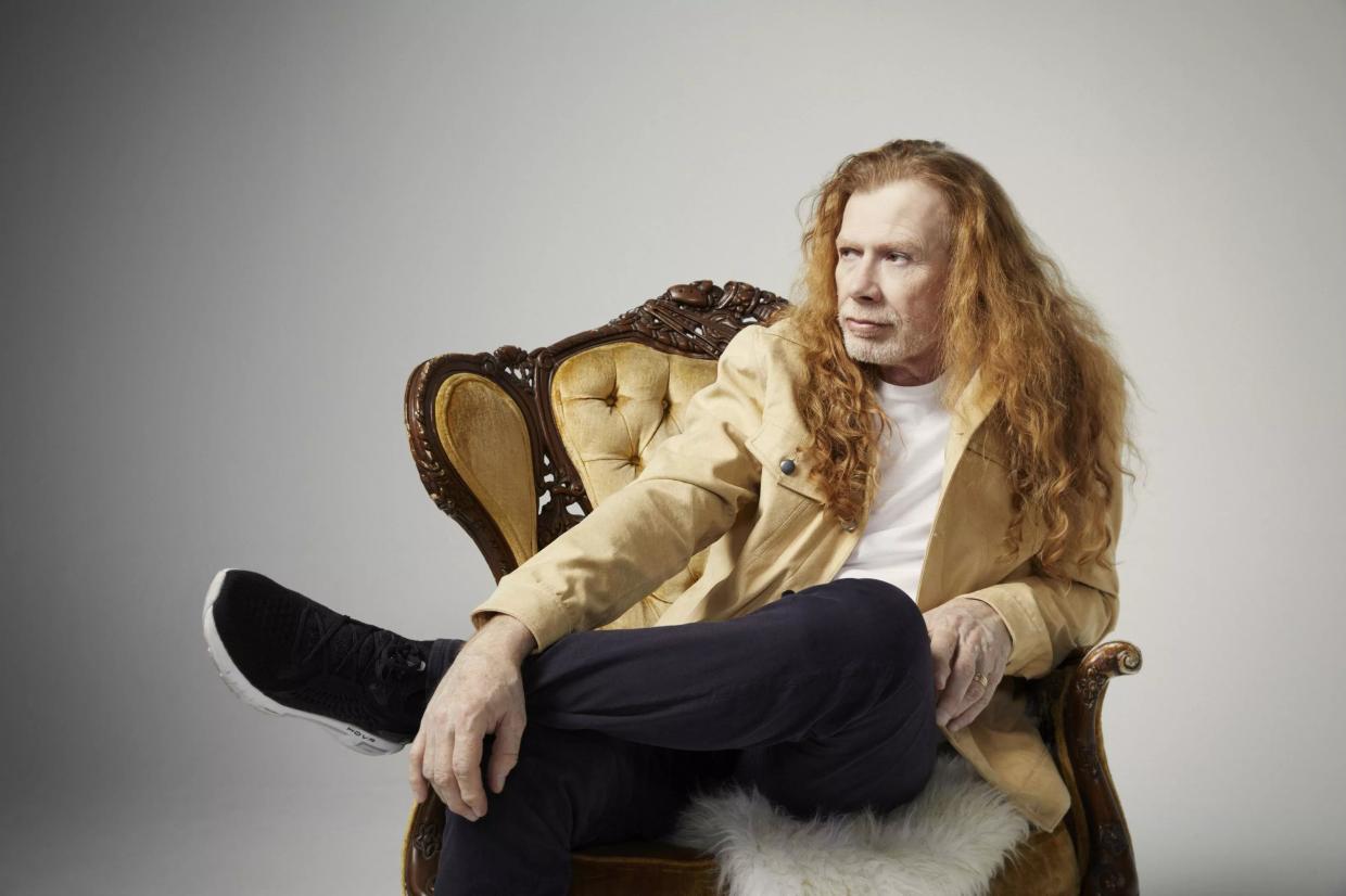 An older man with long hair posing for a photo in a chair.