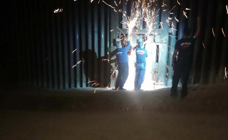firefighters use saws to cut through a border wall