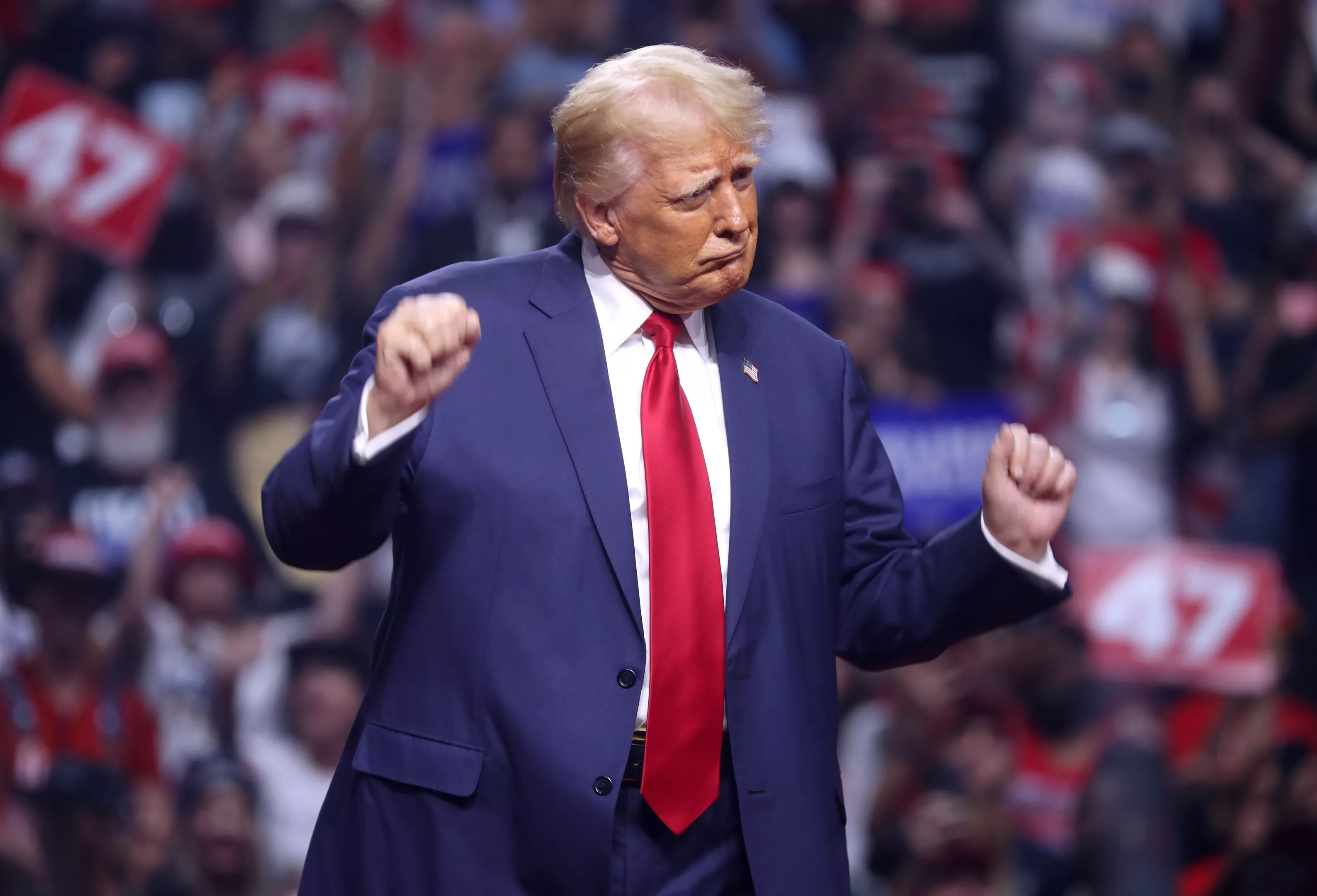 A political candidate in a suit dances in front of a large crowd.