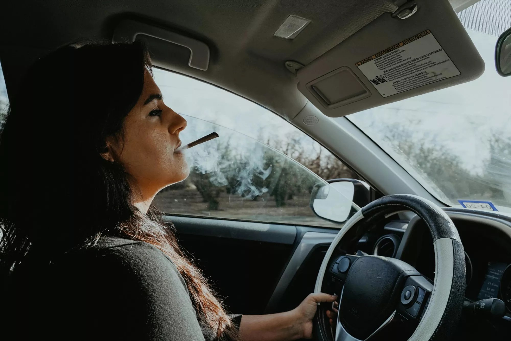 a woman smoking a joint behind the wheel of a car