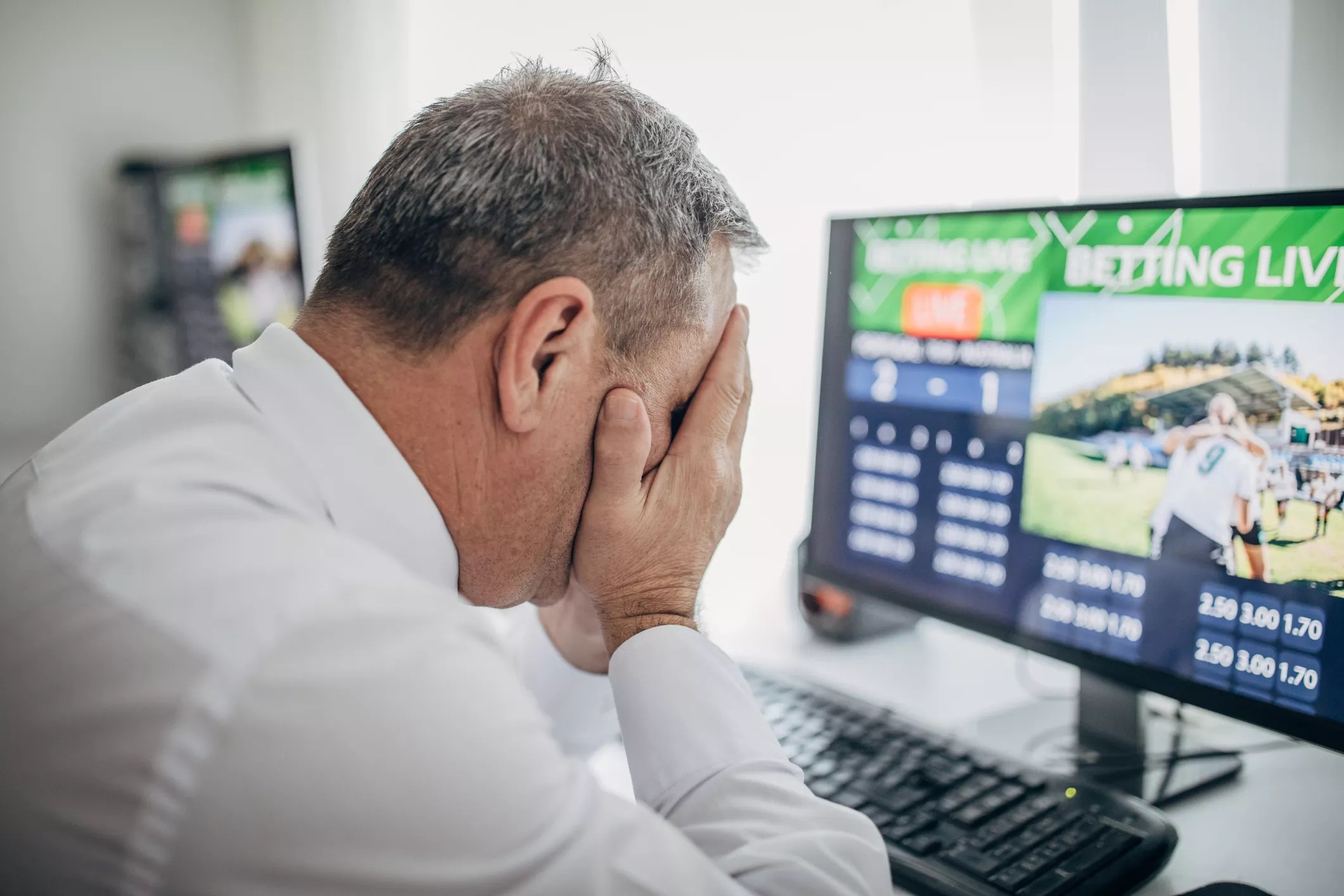 a man puts his head in his hands while looking at a computer screen