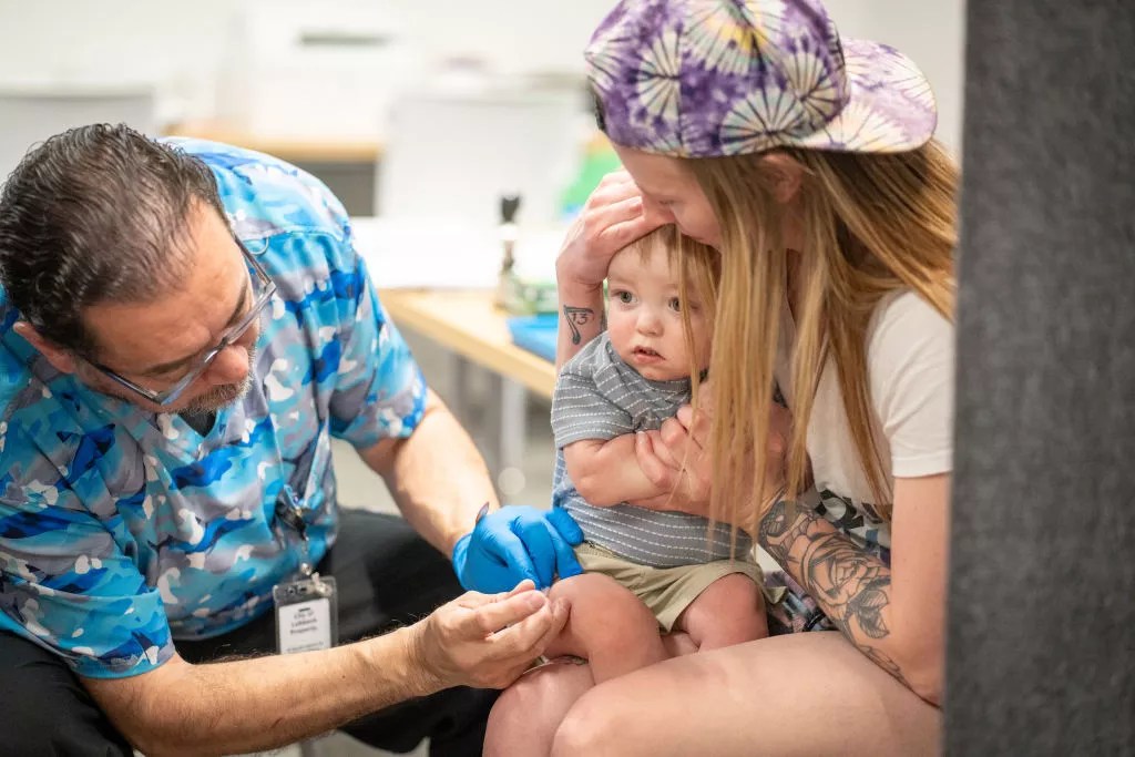 a doctor gives a vaccination shot to an infant sitting in a mother's arms