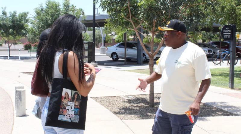 a man in a hat talks to a woman with a tote bag over her shoulder
